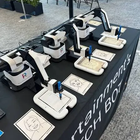 Four robotic arms drawing portrait sketches on a table at an event