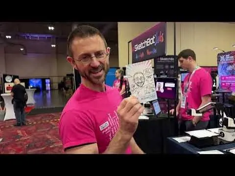 Man in a pink shirt holding up a sketched portrait at an exhibition booth