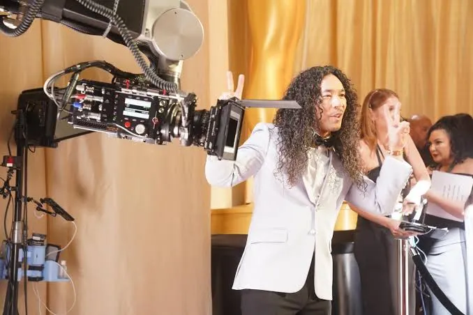 Man in a light suit posing next to a professional robotic camera at a glamorous event