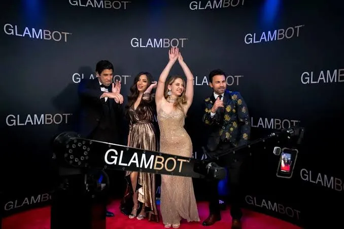Four guests in formal wear posing at a Glambot backdrop on a red carpet