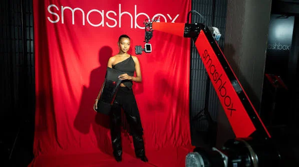Woman posing against a red backdrop while a robotic arm camera films her