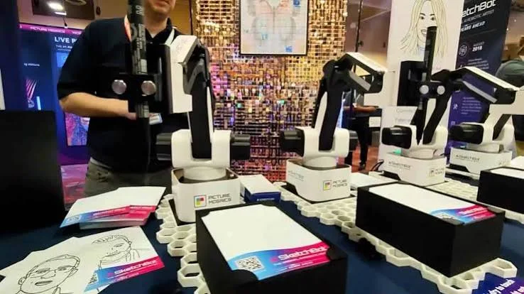 Row of robotic sketch arms and printed portrait sketches at a conference booth