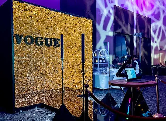 Gold backdrop with rope barriers and a robotic arm camera at an event with coloured lighting